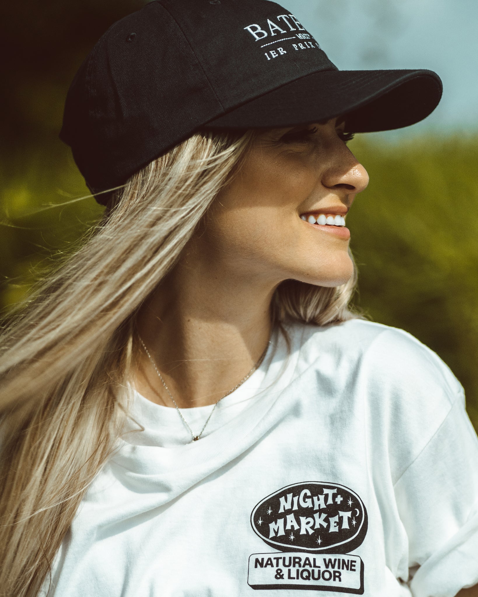 Girl smiling and wearing a Bateau restaurant navy baseball hat and white Night Marketing restaurant t-shirt.